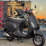 Matzwarte retro-scooter op de standaard voor een showroom, met brandende koplamp.