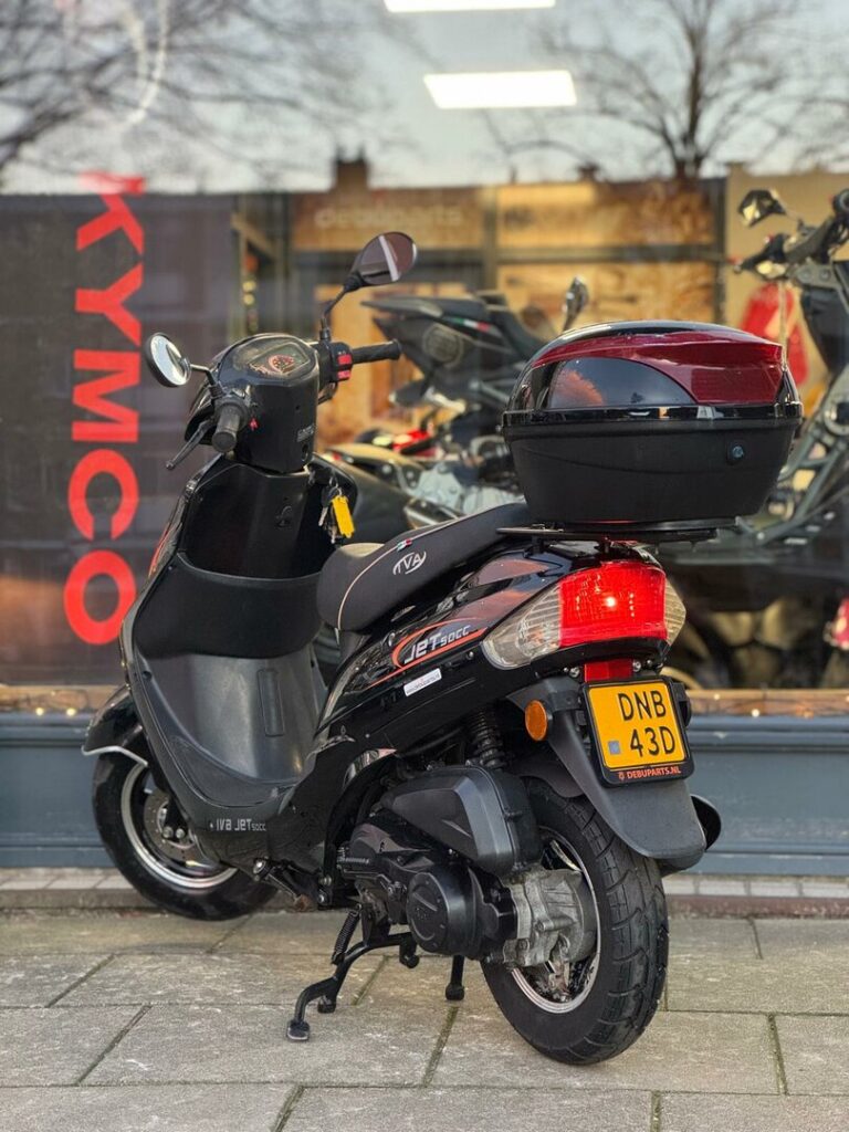 Zwarte scooter met topkoffer geparkeerd voor een motorzaak met KYMCO-logo.