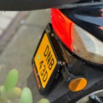 Close-up van de achterkant van een motorfiets met geel kenteken, achterlicht en oranje reflector.