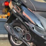 Close-up van de achterzijde van een zwarte 50cc-scooter met uitlaat, achterwiel en zadel.