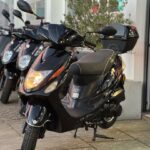 Zwarte scooter met topkoffer op de standaard voor een winkel, koplamp aan