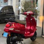 Rode La Souris retro-scooter geparkeerd op nat trottoir voor een garage.