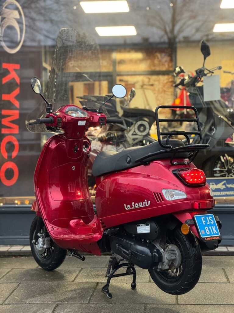 Rode La Souris-scooter met bagagerek voor een motorzaak, geparkeerd op de stoep.