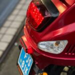 Close-up van de achterzijde van een rode scooter met brandend achterlicht en kentekenplaat.