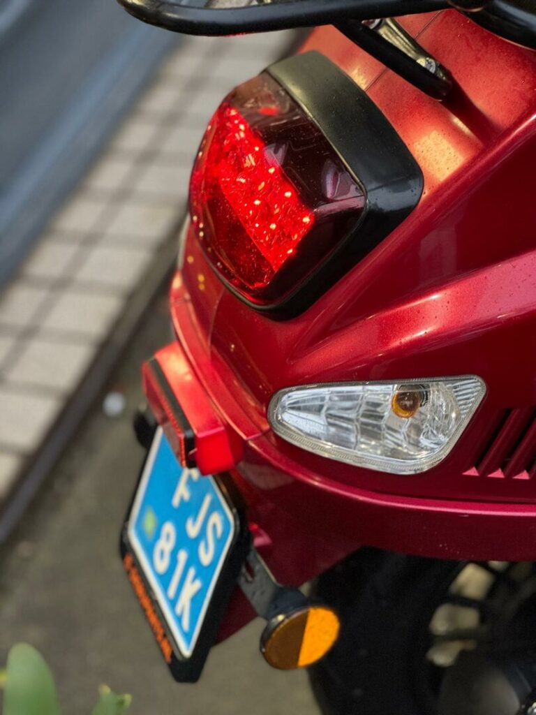 Close-up van de achterzijde van een rode scooter met brandend achterlicht en kentekenplaat.