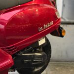 Close-up van de rode La Souris-scooter, met krassen op de zijkap en zicht op zadel en achterwiel.