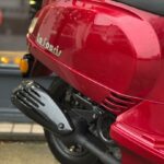 Close-up van rode La Souris scooter met uitlaat en achterwiel op straat.