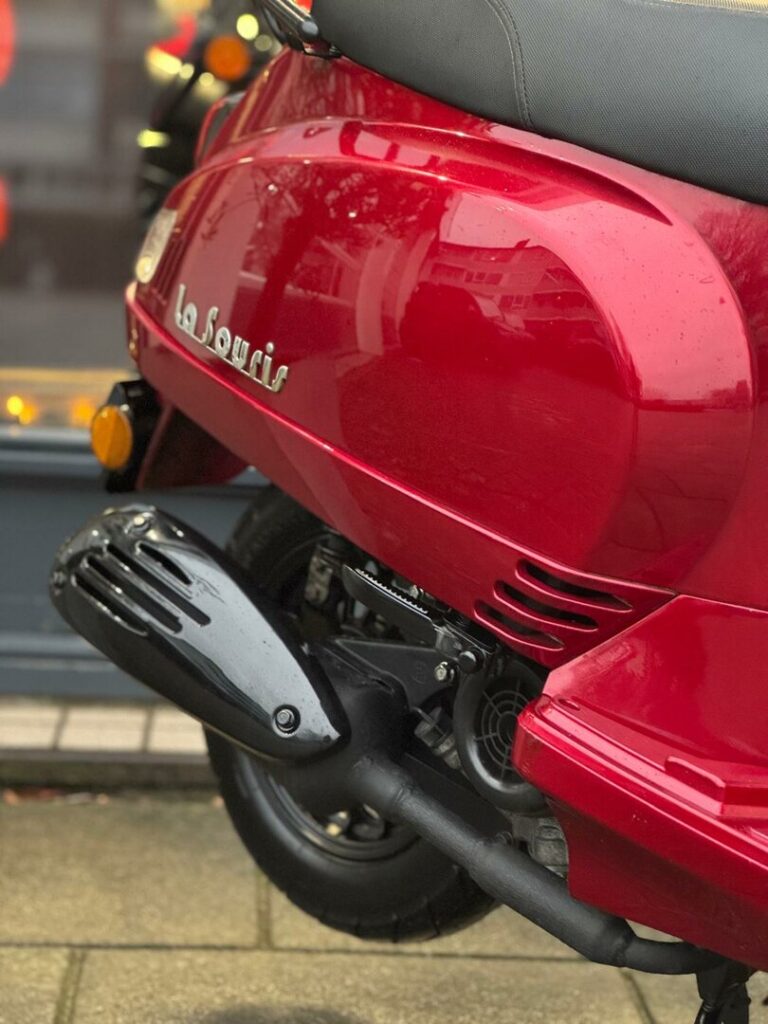 Close-up van rode La Souris scooter met uitlaat en achterwiel op straat.