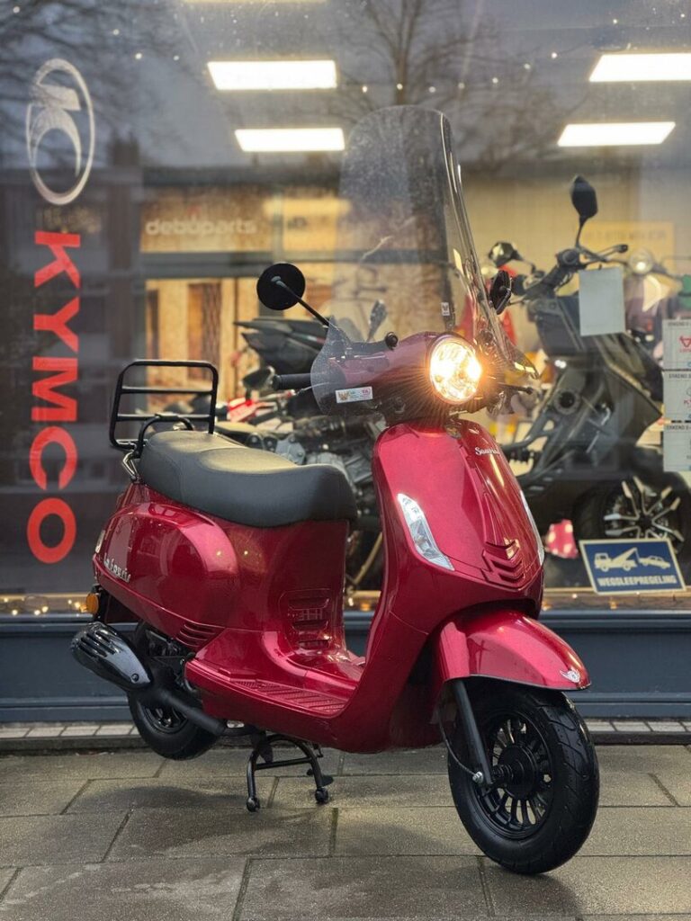 Rode retro-scooter met windscherm voor etalage van Kymco-dealer, koplamp brandt.