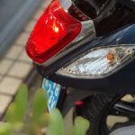 Close-up van het achterlicht en knipperlicht van een scooter, met blauwe kentekenplaat.