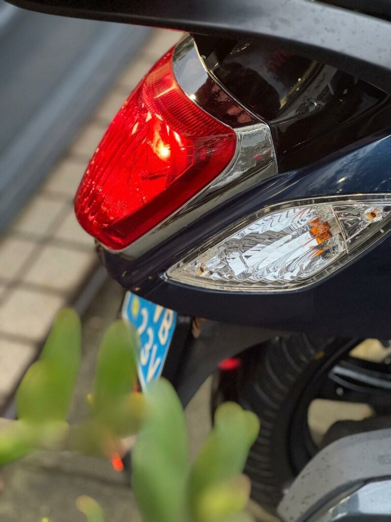 Close-up van het achterlicht en knipperlicht van een scooter, met blauwe kentekenplaat.