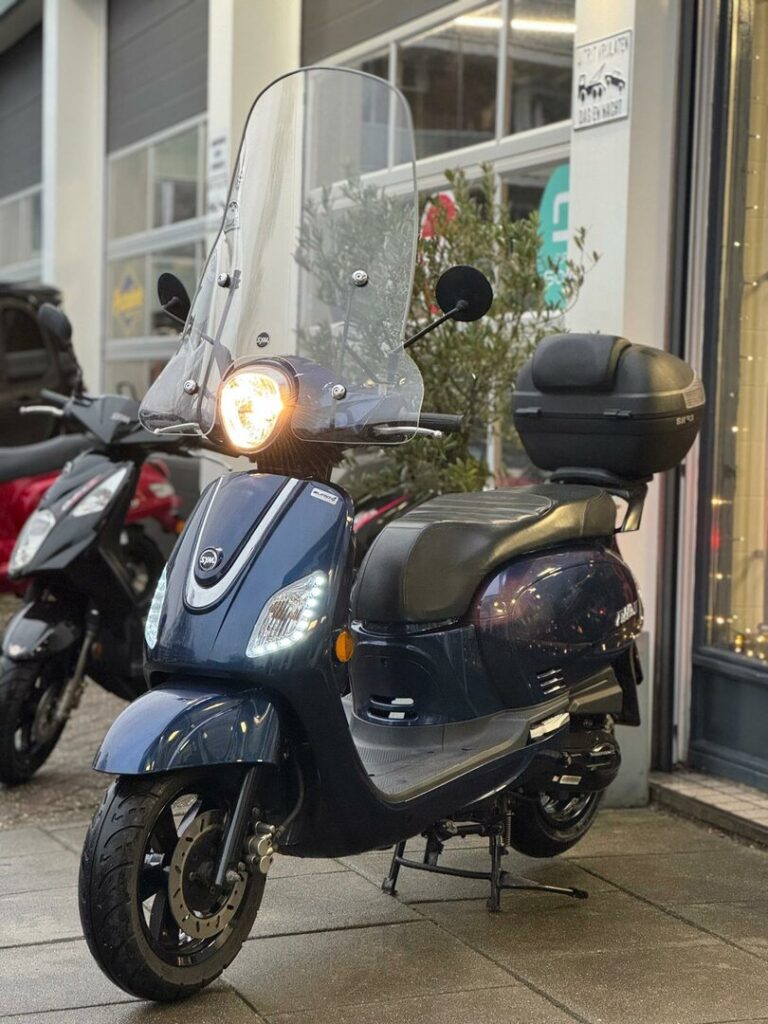 Donkerblauwe scooter met windscherm en topkoffer, geparkeerd voor een winkel.