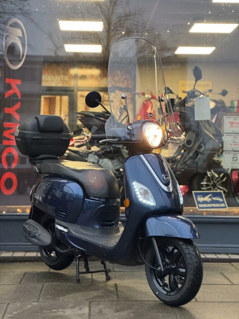 Donkerblauwe scooter met windscherm en topkoffer voor een motorshowroom.
