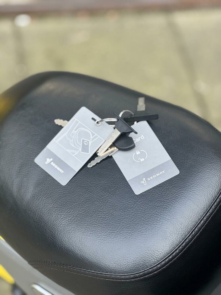 Sleutels met twee Segway-kaarten liggen op een zwart scooterzadel buiten.