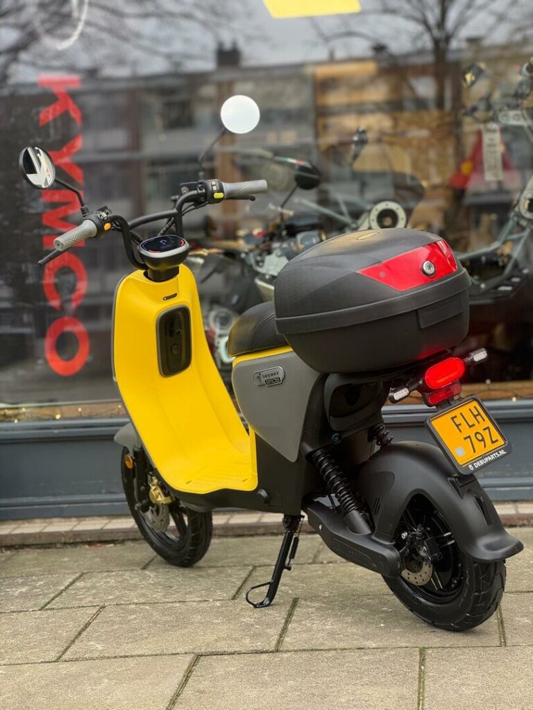 Gele scooter met topkoffer geparkeerd voor een winkelraam met KYMCO-tekst.