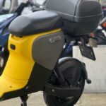 Close-up van de achterzijde van een gele Segway e-scooter met topkoffer, op de standaard geparkeerd.