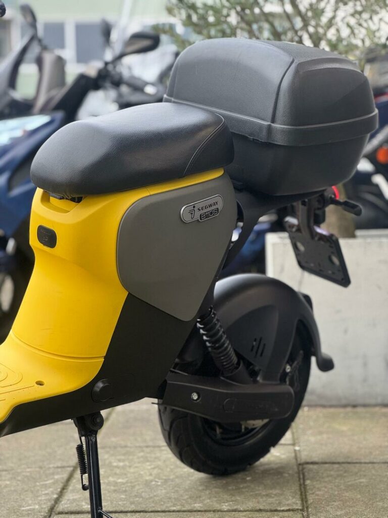 Close-up van de achterzijde van een gele Segway e-scooter met topkoffer, op de standaard geparkeerd.