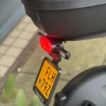 Achterkant van een scooter met topkoffer, brandend achterlicht en gele kentekenplaat.