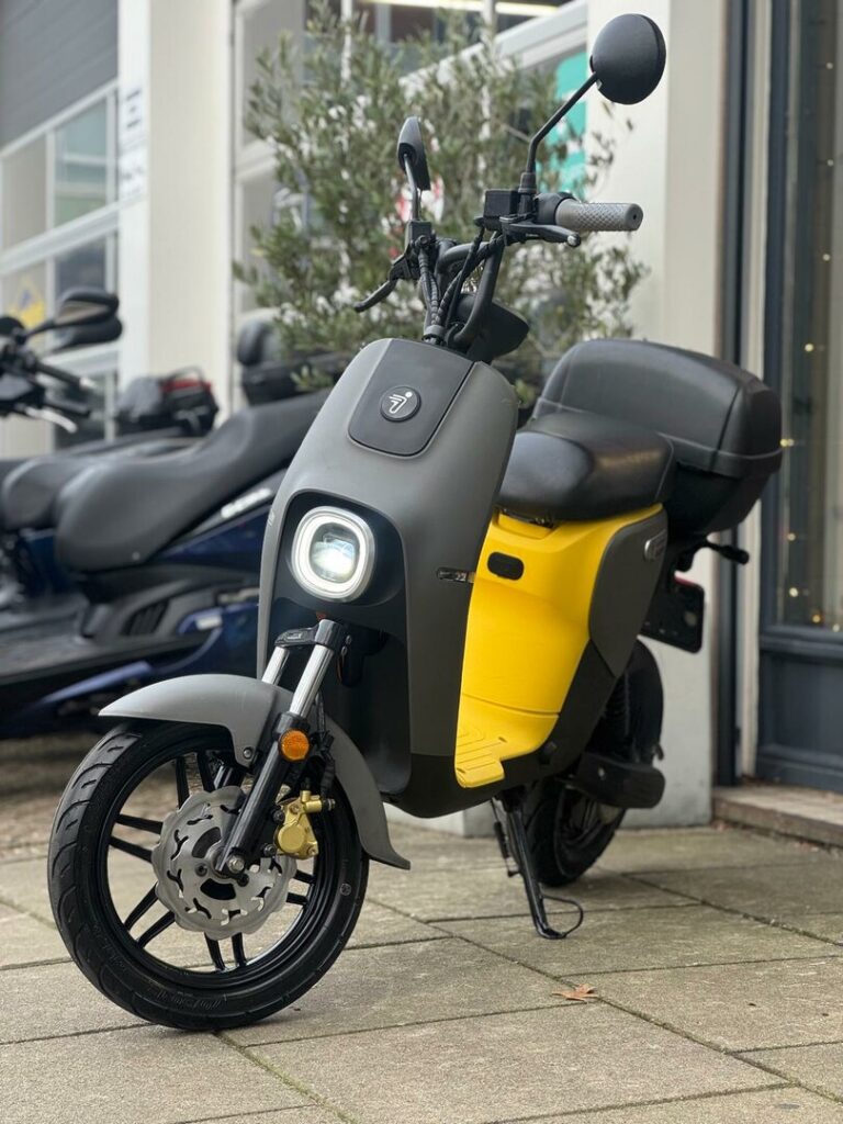 Zwart-gele elektrische scooter met ronde koplamp geparkeerd op stoep voor winkel