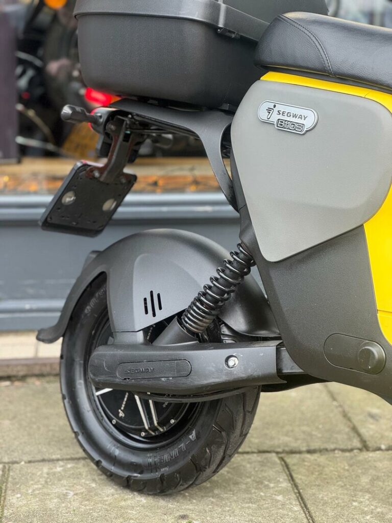 Close-up van het achterwiel en de vering van een gele Segway B110S e-scooter.