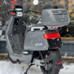 Grijze NIU elektrische scooter met topkoffer, geparkeerd in de sneeuw