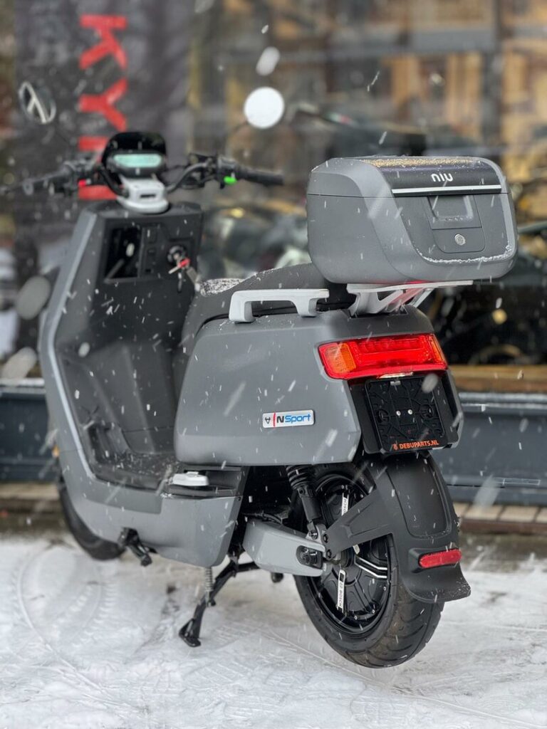 Grijze NIU elektrische scooter met topkoffer, geparkeerd in de sneeuw