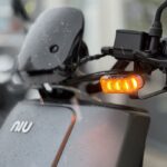 Close-up van een NIU-scooter met brandend knipperlicht en regendruppels.
