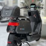 Zwarte elektrische NIU-scooter met topkoffer in de sneeuw, close-up van achterkant.