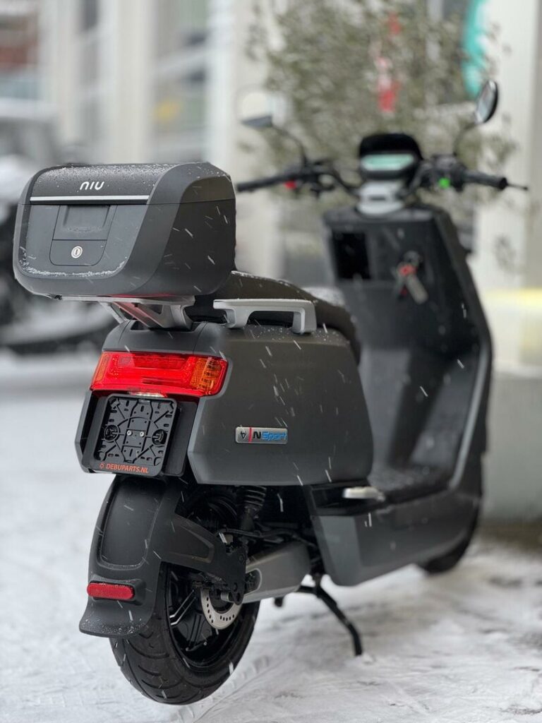 Zwarte elektrische NIU-scooter met topkoffer in de sneeuw, close-up van achterkant.