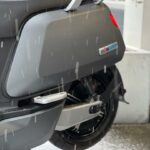 Close-up van het achterwiel en zijkant van een grijze scooter met voetsteun, in natte sneeuw.