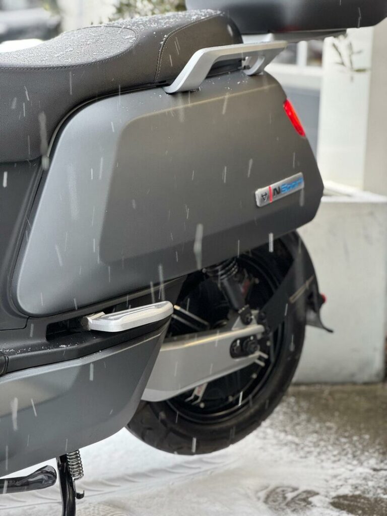 Close-up van het achterwiel en zijkant van een grijze scooter met voetsteun, in natte sneeuw.