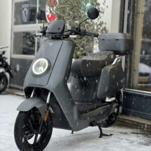 Grijze elektrische NIU-scooter met topkoffer geparkeerd buiten in de sneeuw
