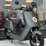 Grijze elektrische scooter met topkoffer geparkeerd in de sneeuw voor een winkel