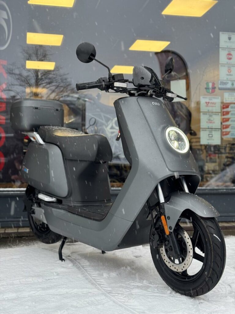 Grijze elektrische scooter met topkoffer geparkeerd in de sneeuw voor een winkel