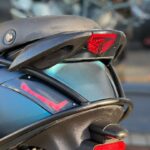 Close-up van het achterdeel van een motorfiets met rode LED-achterlichten en een metallic groenblauwe kuip.