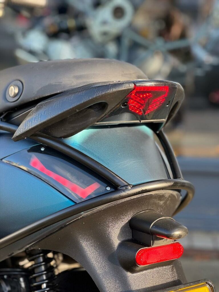 Close-up van het achterdeel van een motorfiets met rode LED-achterlichten en een metallic groenblauwe kuip.