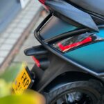 Detail van de achterzijde van een scooter met zadel, achterlicht en geel kenteken.