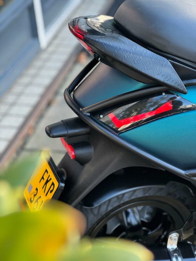 Detail van de achterzijde van een scooter met zadel, achterlicht en geel kenteken.