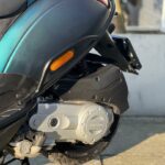 Close-up van de achterzijde van een scooter met Piaggio-motor, veer en achterwiel in warm zonlicht.