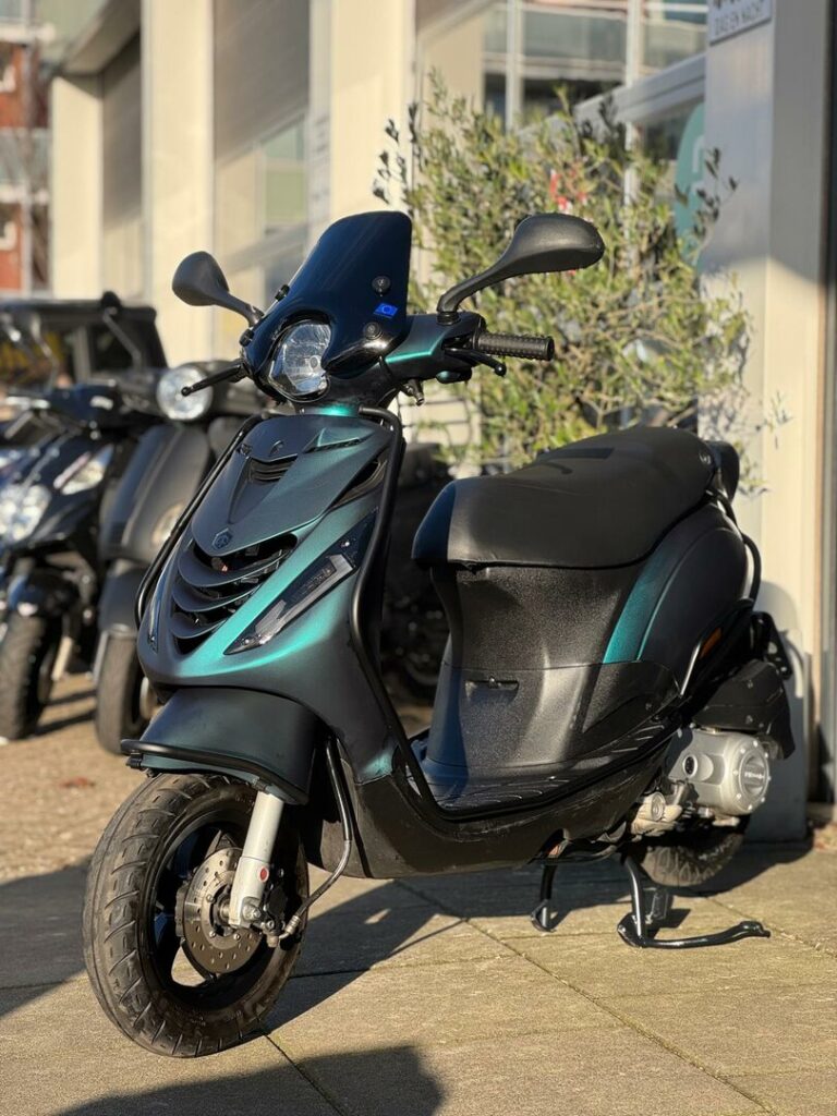 Zwarte scooter met groen metallic accenten, op standaard geparkeerd buiten bij een showroom.