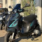 Zwart-groene scooter met windscherm op standaard, geparkeerd voor een winkel.