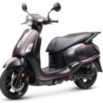 Mat zwarte retro-scooter met ronde koplamp en brede zitting, driekwart vooraanzicht op witte achtergrond.