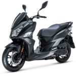 Zwarte, sportieve scooter met dubbele koplampen op witte achtergrond, schuin van voren gefotografeerd.