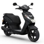 Matzwarte stadscooter met groot voorlicht, driekwart vooraanzicht op witte achtergrond.