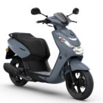 Grijze stadsscooter met zwart zadel en zwarte velgen, driekwart vooraanzicht op witte achtergrond.