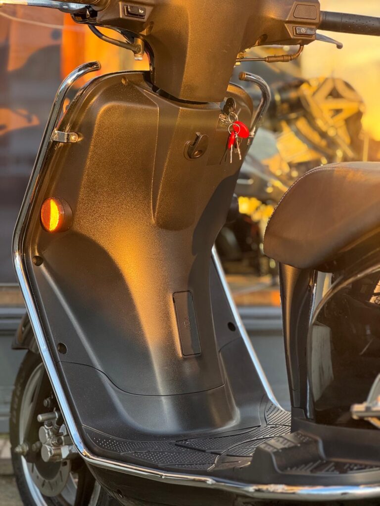 Close-up van de voetenruimte van een scooter met sleutels in het contact, in warm avondlicht