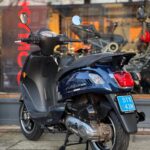 Donkerblauwe scooter met blauwe kentekenplaat, geparkeerd voor een winkel met glazen pui.