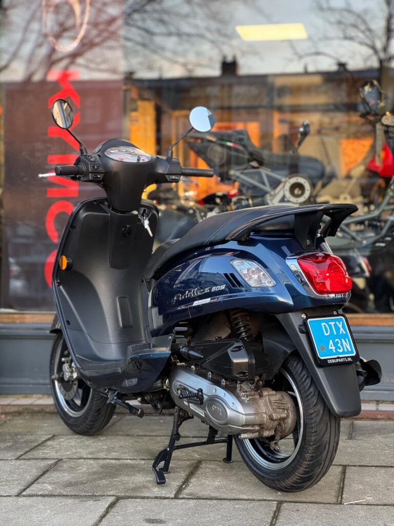 Donkerblauwe scooter met blauwe kentekenplaat, geparkeerd voor een winkel met glazen pui.