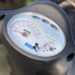 Close-up van het instrumentenpaneel van een SYM scooter met snelheidsmeter en brandstofmeter.