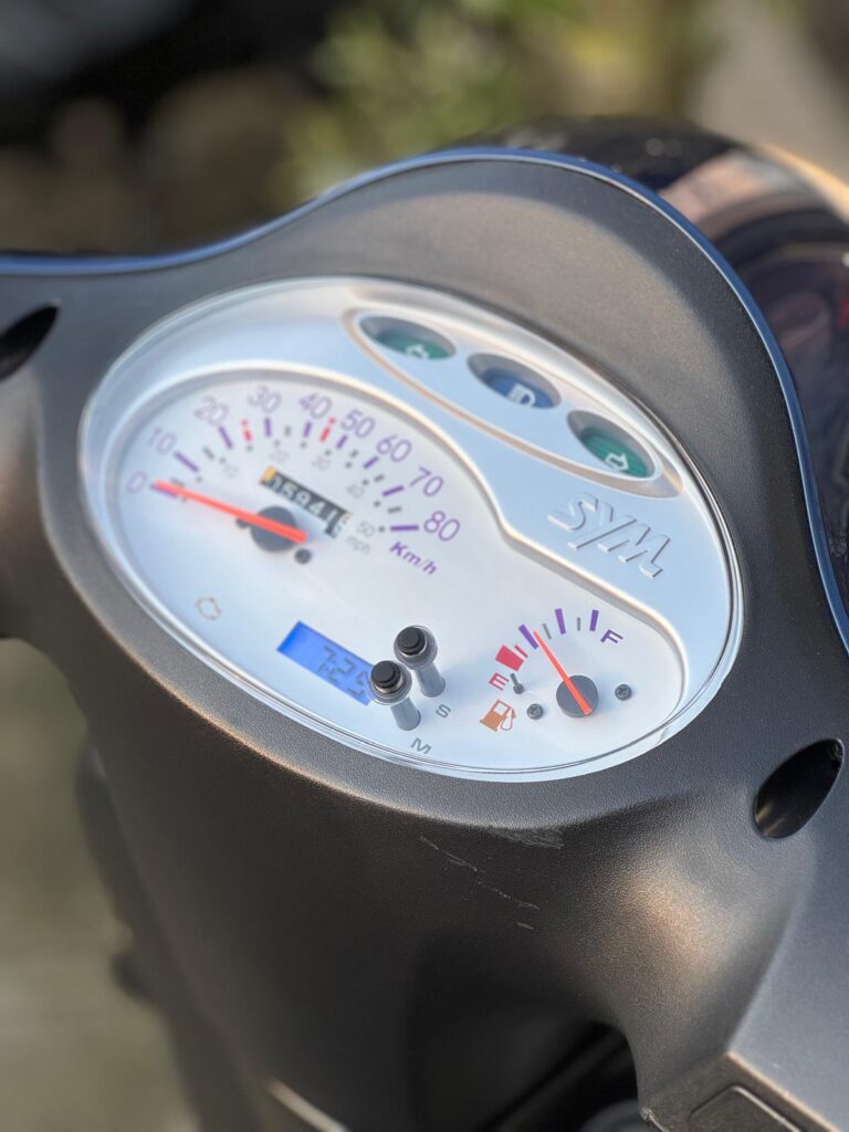 Close-up van het instrumentenpaneel van een SYM scooter met snelheidsmeter en brandstofmeter.